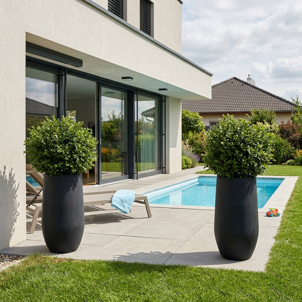Detail na matně černý betonový květináč Zenith XXL (40x80 cm) s keřem na moderní rodinné terase s bazénem.